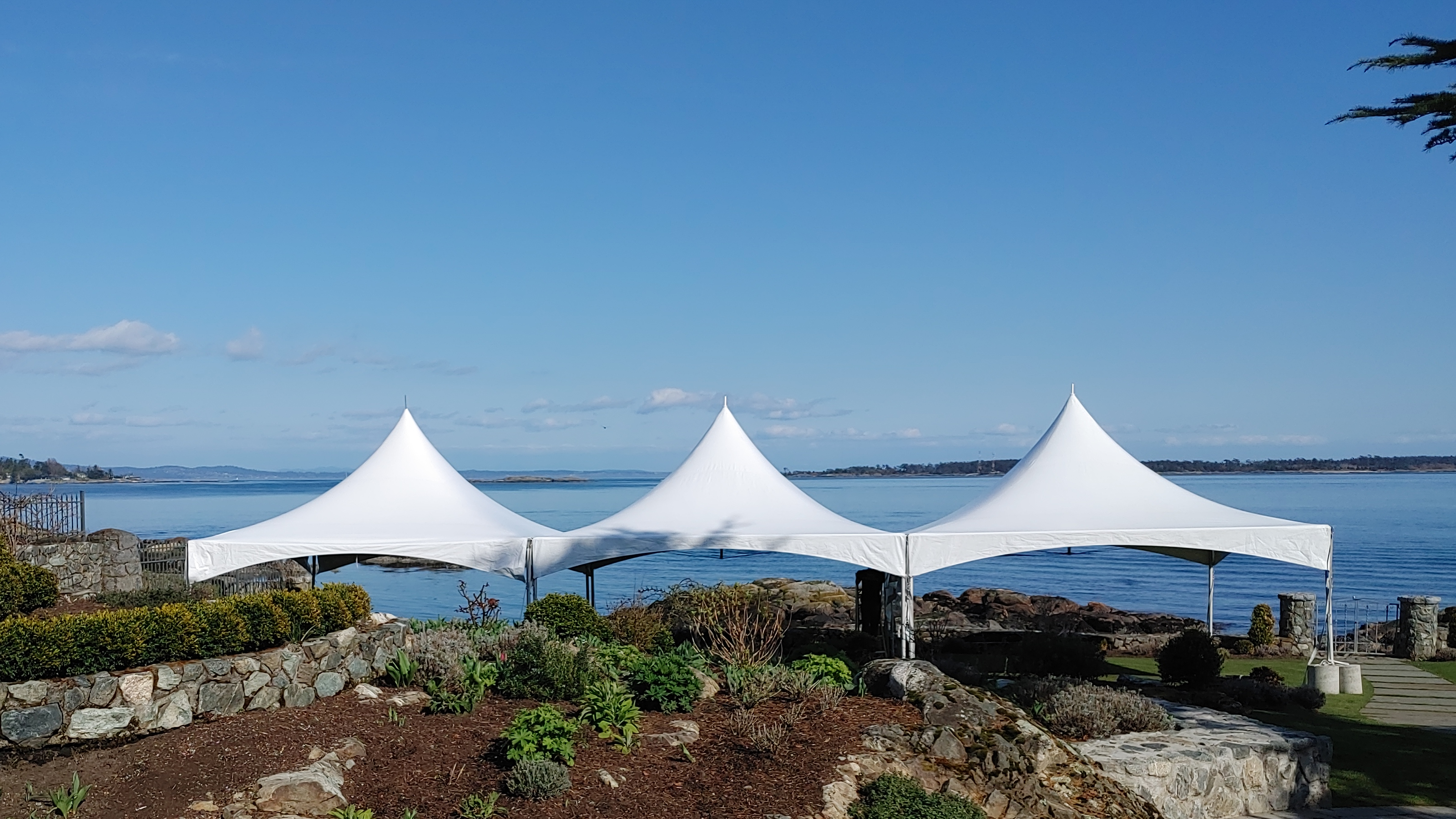 Three white marquee tents set up on a stone terrace above the sea